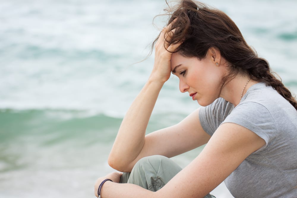 Sad and upset woman deep in thought Woman sitting at beachside having anxiety due to bulging veins