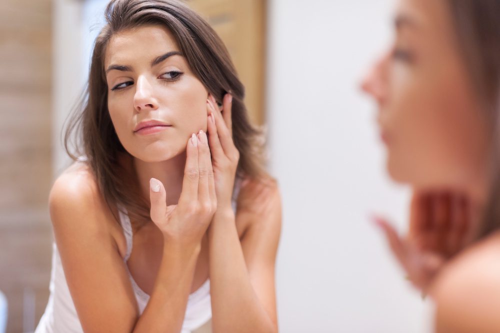 Can Botox Help Treat Acne? woman looking in the mirror debating on botox and if it will help her acne
