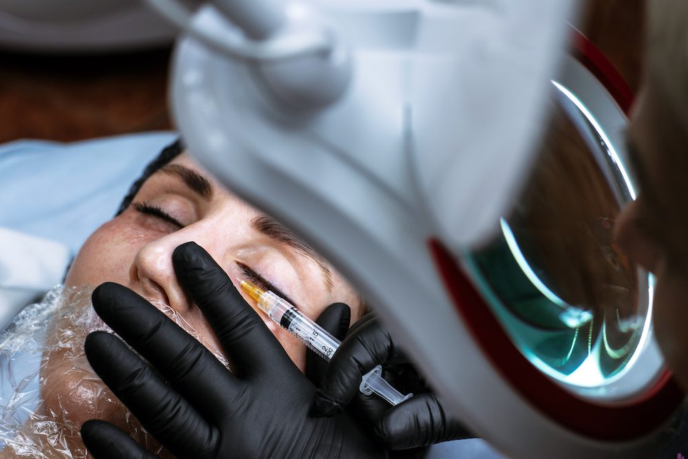 Your Guide to Under Eye Fillers Beautician makes an injection of beauty. The doctor injects an injection under the eyes of a young woman. Cosmetologist services.